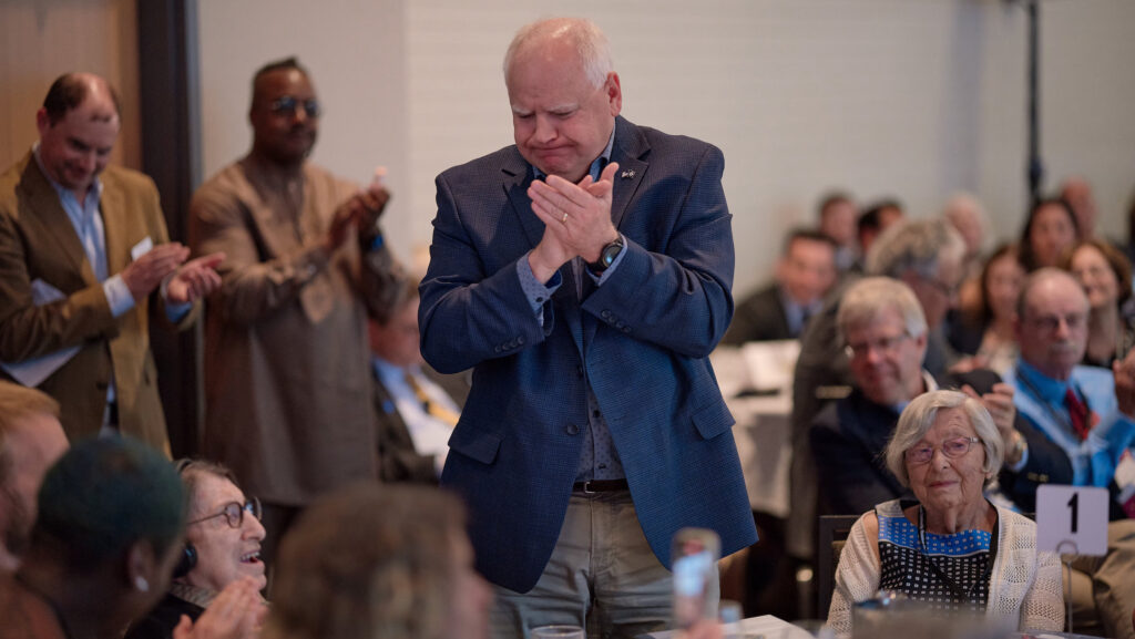 A politician stands and applauds an elderly woman at a gala dinner