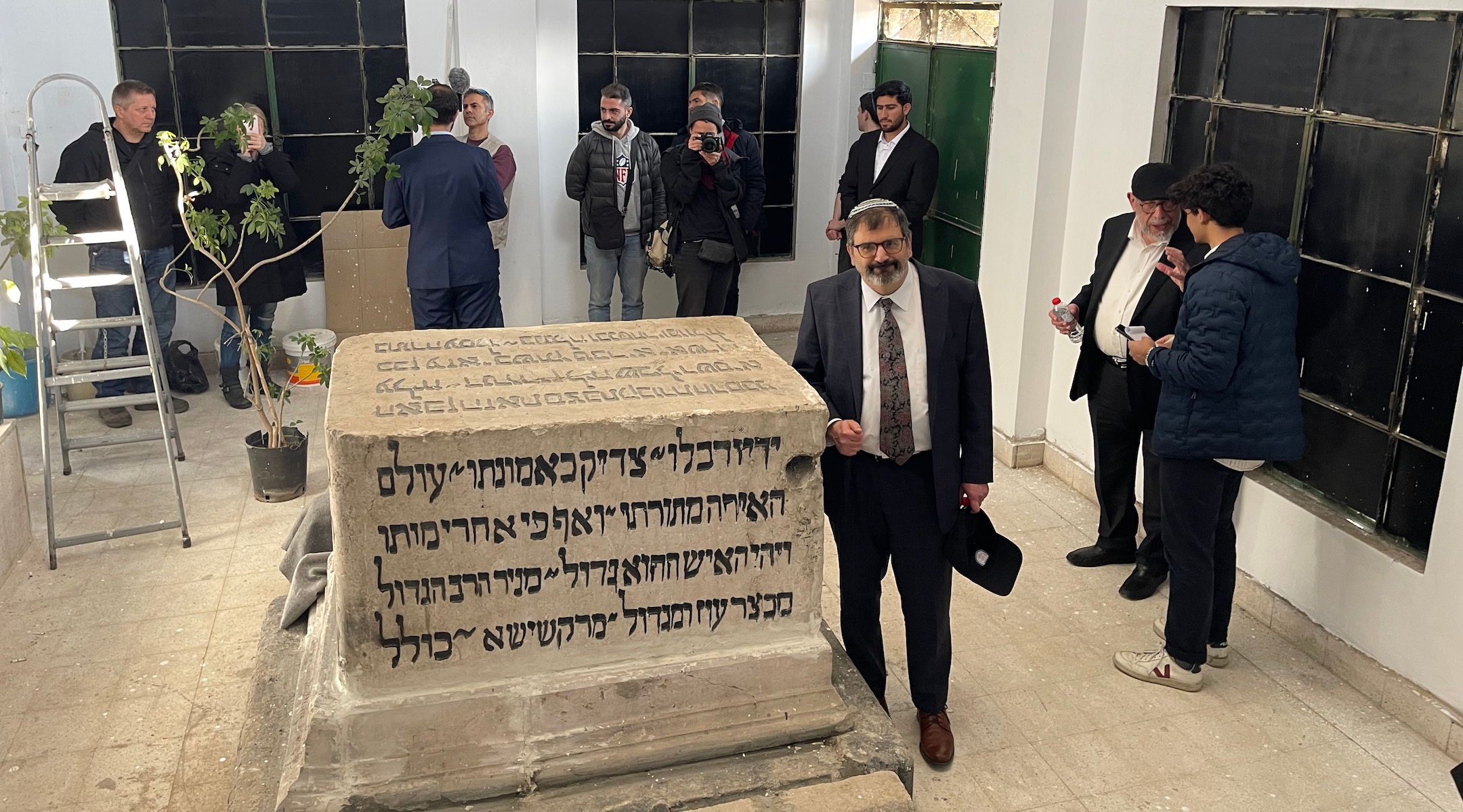 A rabbi poses next to a large headstone with Hebrew inscriptions in Syria