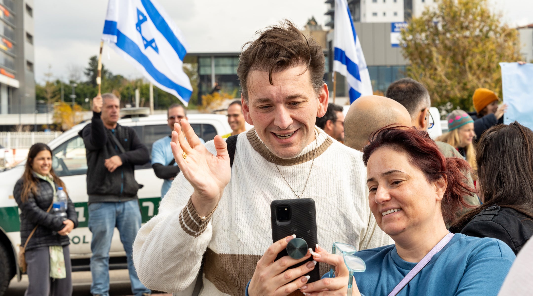 A photo of a man waving at a phone.