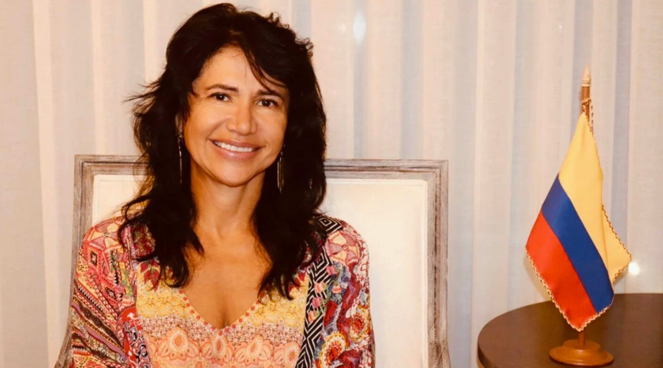 A photo of a woman smiling next to a flag.